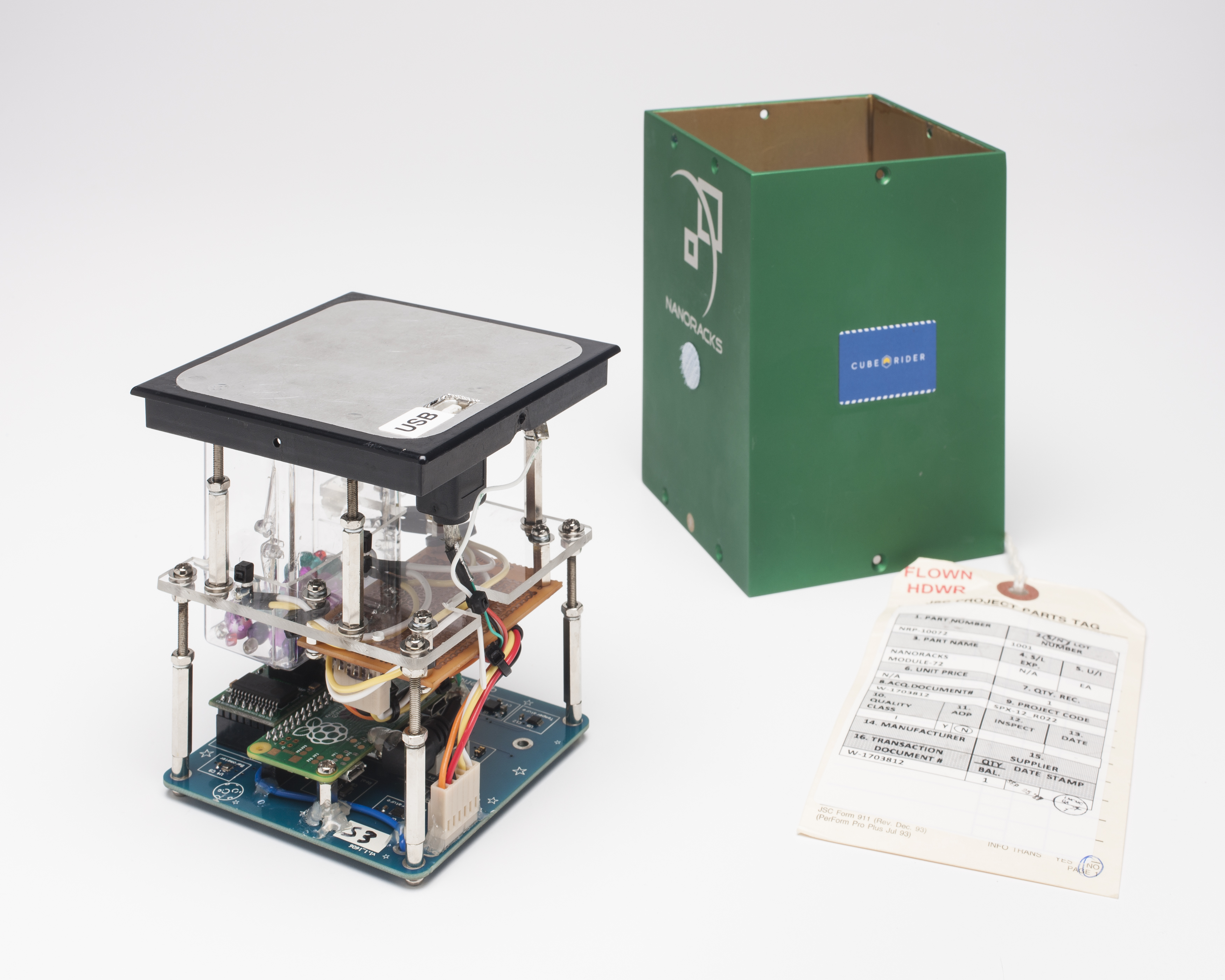 A rectangular unit about 15cm high, comprising a series of electronics. On the right is a green metal case for the device, and attached to it a paper label stamped with the words 'FLOWN HDWR'.